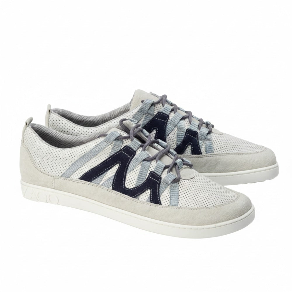 Ein Paar DRAQE White Grey Sneaker von ZAQQ aus Premium Nappaleder, mit perforierter Textur und dunkelblauen Zickzack-Streifen. Hellgraue Schnürsenkel betonen das Design und die flache Sohle weist ein geprägtes Branding an der Ferse auf. Die Schuhe sind von der Seite abgebildet und stehen für raffinierte Eleganz.
