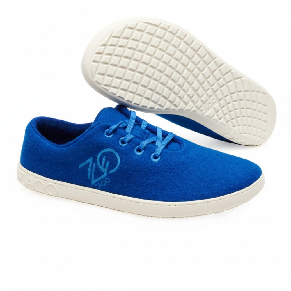 Die LIQE Azur Sneaker von ZAQQ zeichnen sich durch ein elegantes Design mit blauem Obermaterial und weißer Sohle aus, akzentuiert durch ein Logo an der Seite. Diese Sneaker sind für den Komfort ähnlich wie Barfußschuhe konzipiert und verfügen über blaue Schnürsenkel. Ein Sneaker wird in einer Seitenansicht gezeigt, während der andere seine strukturierte Sohle nach vorne zeigt.