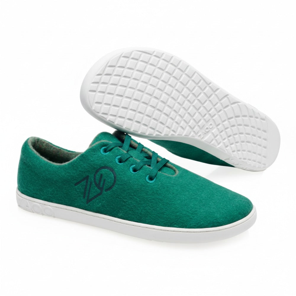 Ein Paar LIQE Green Casual Sneakers von ZAQQ mit weißer Sohle. Ein Schuh liegt flach, während der andere die Sohle mit Gittermuster zeigt. Das Logo ist sowohl an der Seite als auch an der Sohle zu sehen und unterstreicht den modernen Stil eines Barfußschuhs.