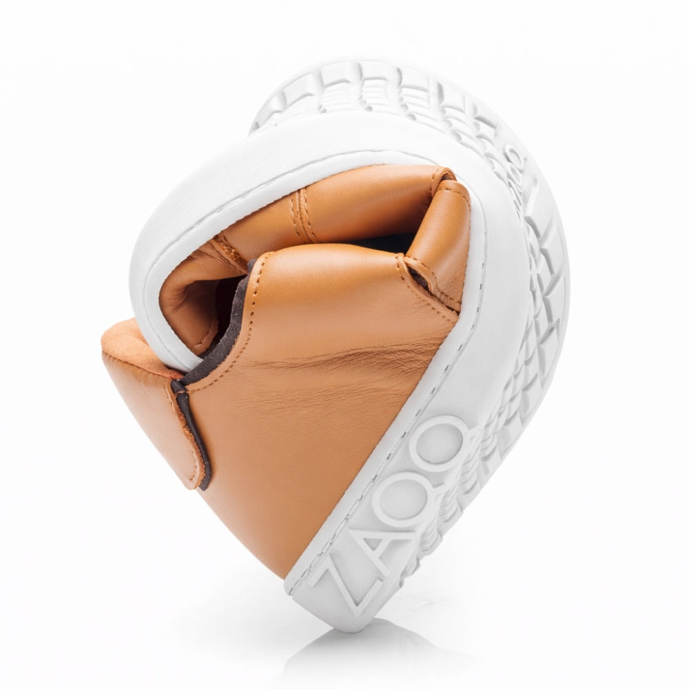 Der QQQ Low Sierra, ein flexibler Barfußschuh von ZAQQ, verfügt über hellbraunes Nappaleder und eine weiße Sohle, die sich zu einer Kugel zusammenfalten lässt und so ihre Biegsamkeit demonstriert. Der Markenname ZAQQ ist auf der flexiblen Kautschuksohle eingeprägt.