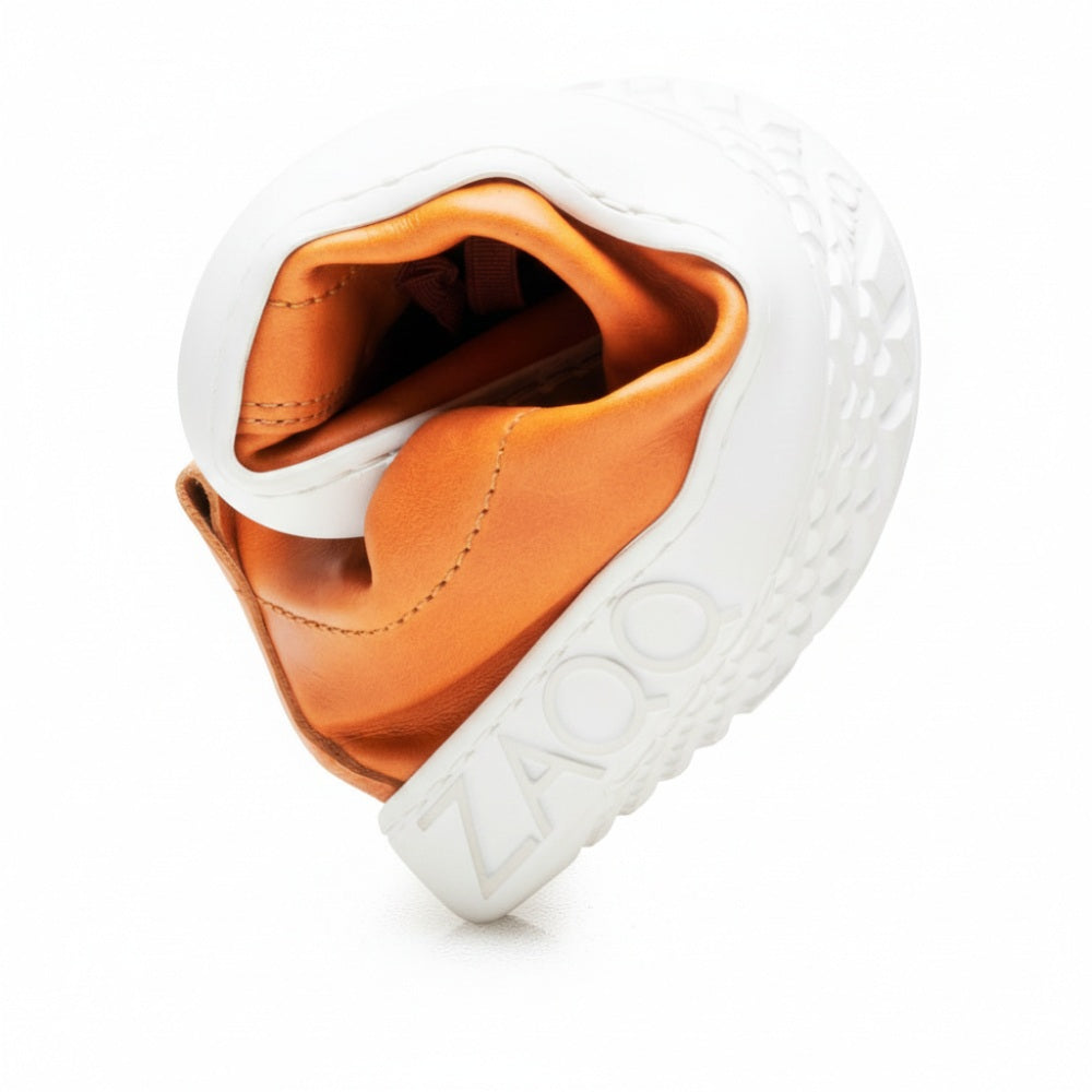 Ein anpassungsfähiger orange-grauer Sneaker, bekannt als STIQ Sierra, ist kreisförmig gebogen, um sein weiches Nappaledermaterial und seine strukturierte Sohle hervorzuheben. Der Markenname ZAQQ ist prominent auf der Sohle angebracht und unterstreicht die Qualität dieses Barfußschuh-Designs.